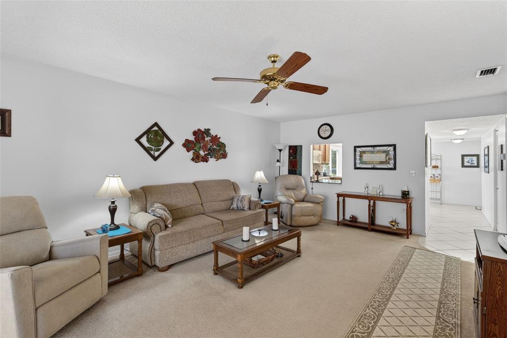 A living room features beige carpet, a ceiling fan, a television, and sliding glass doors — 6699 SAN CASA DRIVE UNIT L8, ENGLEWOOD, FL
