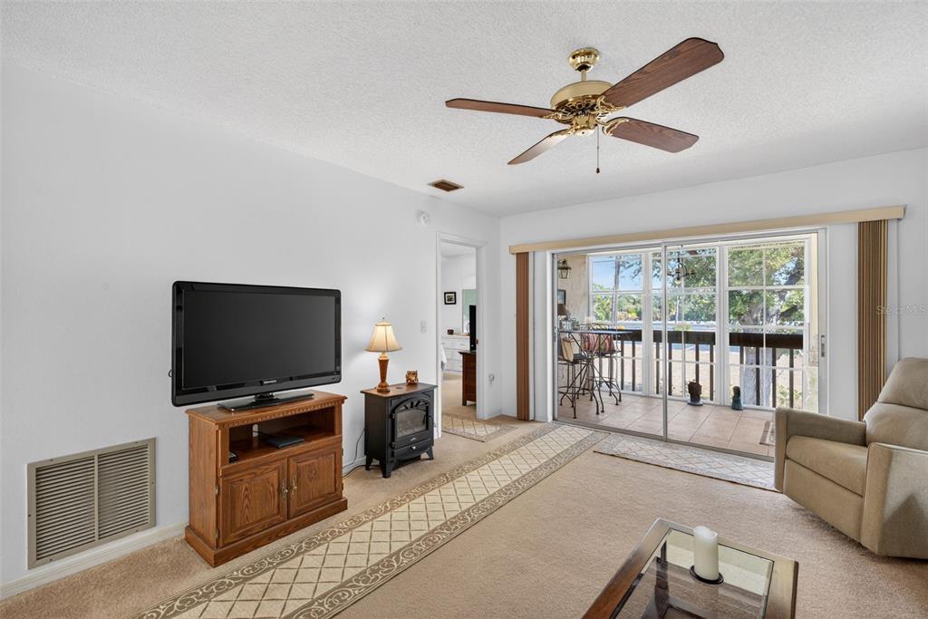 A living room features beige carpet, a ceiling fan, a television console, and a fireplace — 6699 SAN CASA DRIVE UNIT L8, ENGLEWOOD, FL