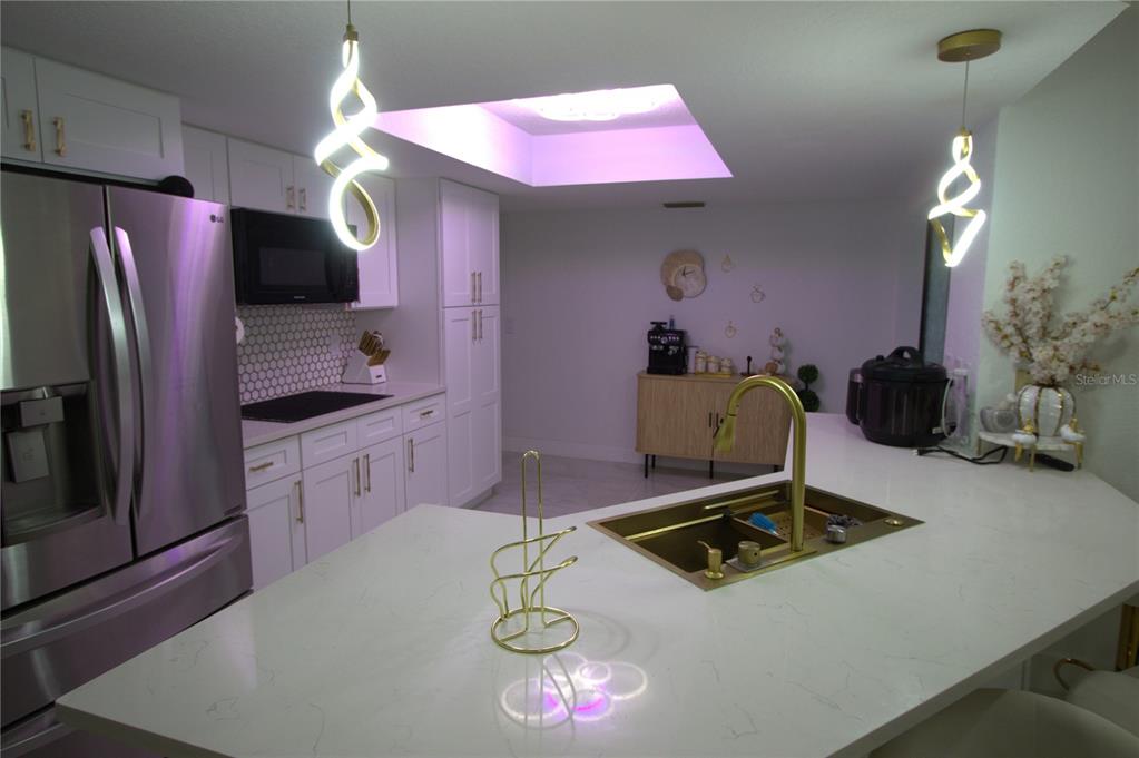 A modern kitchen features white cabinetry, quartz countertops, gold fixtures, and two unique pendant lights — 5045 KENMORE STREET, SPRING HILL, FL