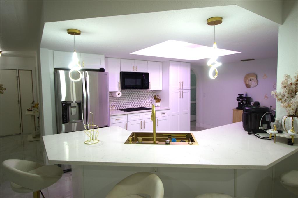 A modern kitchen features white cabinetry, a gold sink, and a large quartz peninsula island — 5045 KENMORE STREET, SPRING HILL, FL