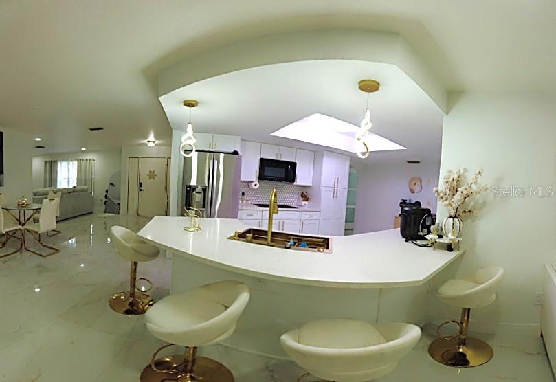 A kitchen features a curved white island with gold accents and modern pendant lighting — 5045 KENMORE STREET, SPRING HILL, FL