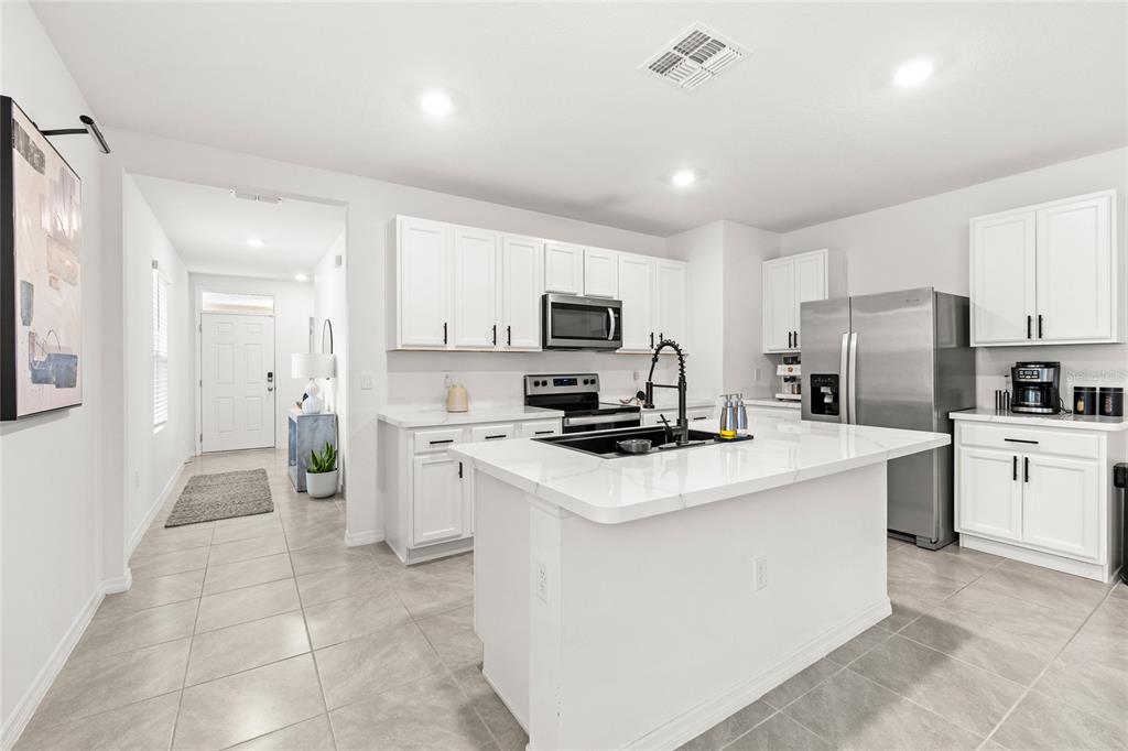 A bright kitchen features white cabinets, a central island with a sink, and stainless appliances — 1663 ROSYDALE CIRCLE, DAVENPORT, FL