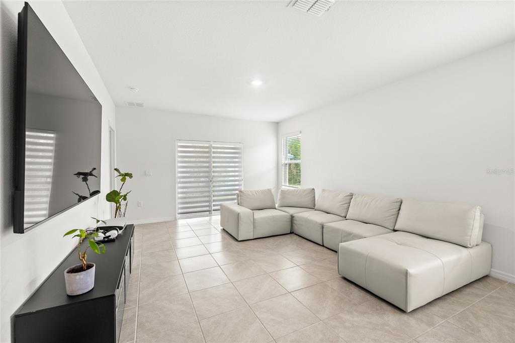 A living room features light tile flooring, a large sectional sofa, and a wall-mounted television — 1663 ROSYDALE CIRCLE, DAVENPORT, FL