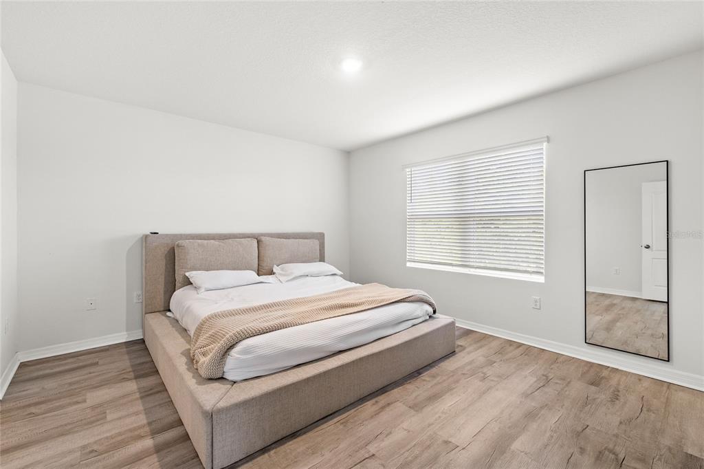 A bedroom features a beige upholstered bed, light wood-look flooring, and a full-length wall mirror — 1663 ROSYDALE CIRCLE, DAVENPORT, FL