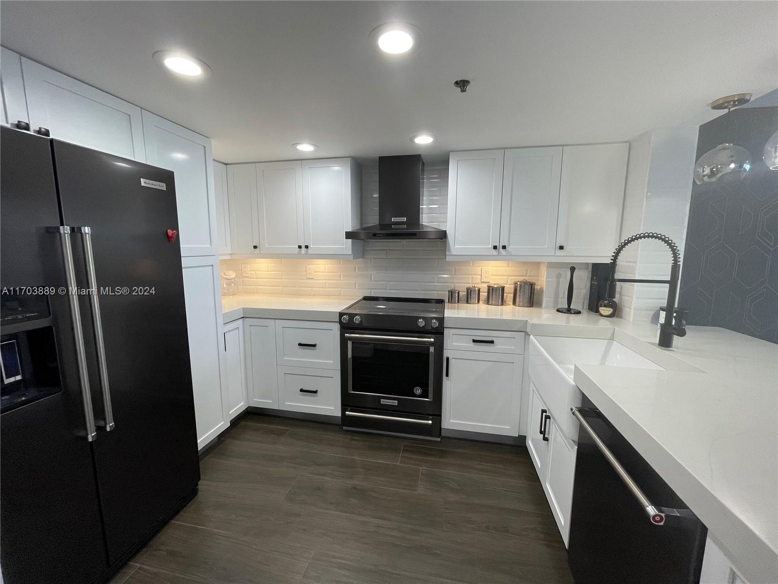 A modern kitchen features white cabinets, black appliances, a farmhouse sink, and dark wood flooring — 2555 Collins Ave # 1409, Miami Beach FL 33140, MIAMI BEACH, FL