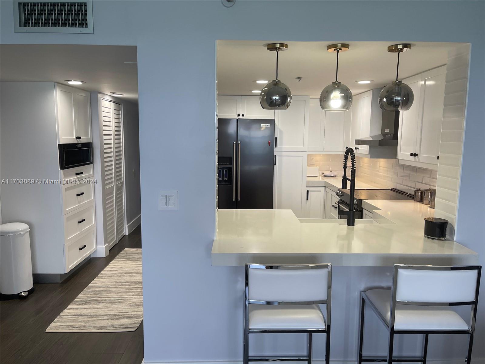 A modern kitchen features white cabinetry, a breakfast bar with stools, and dark stainless appliances — 2555 Collins Ave # 1409, Miami Beach FL 33140, MIAMI BEACH, FL