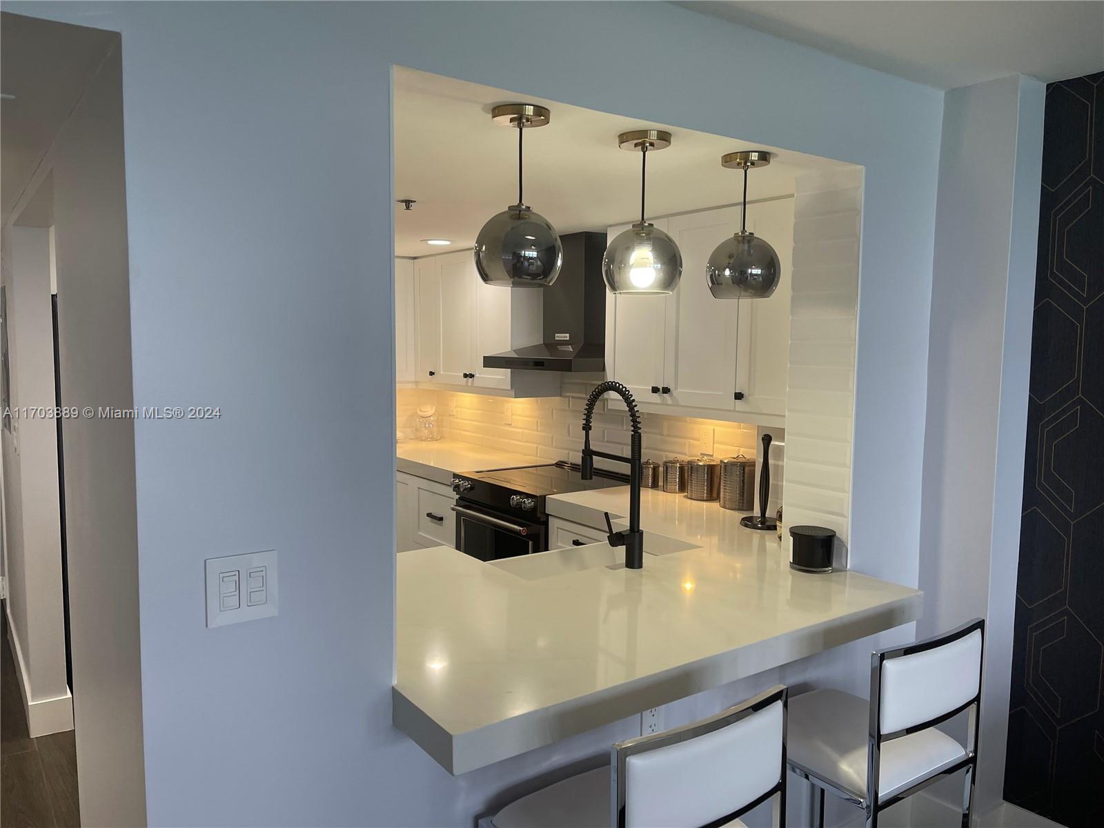 A kitchen with white cabinets, quartz countertops, and three pendant lights over a breakfast bar — 2555 Collins Ave # 1409, Miami Beach FL 33140, MIAMI BEACH, FL