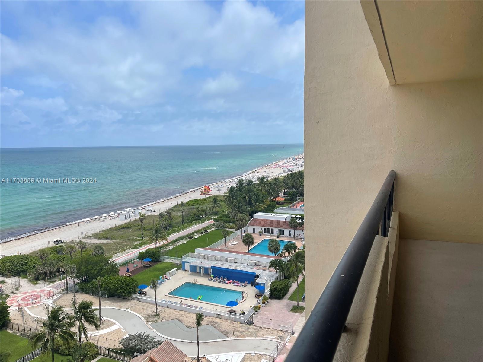 A high-angle view from a balcony overlooks a beach, swimming pools, and palm trees — 2555 Collins Ave # 1409, Miami Beach FL 33140, MIAMI BEACH, FL