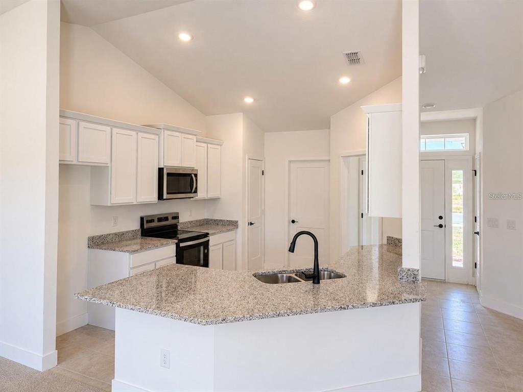 A kitchen features white cabinets, granite countertops, a black faucet, and stainless steel appliances — 1684 ANN ROSE WAY, LEESBURG, FL