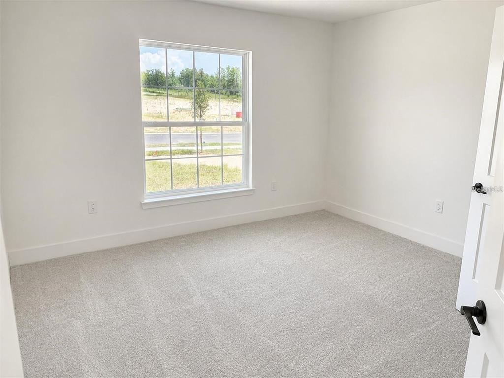An empty bedroom with white walls, gray carpet, and a window overlooking a grassy area — 1684 ANN ROSE WAY, LEESBURG, FL