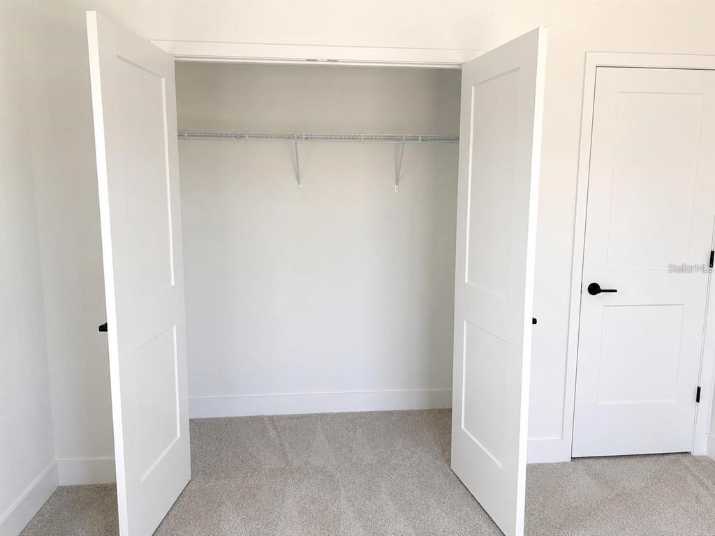 A bedroom features a white double-door closet with wire shelving and a closed door nearby — 1684 ANN ROSE WAY, LEESBURG, FL