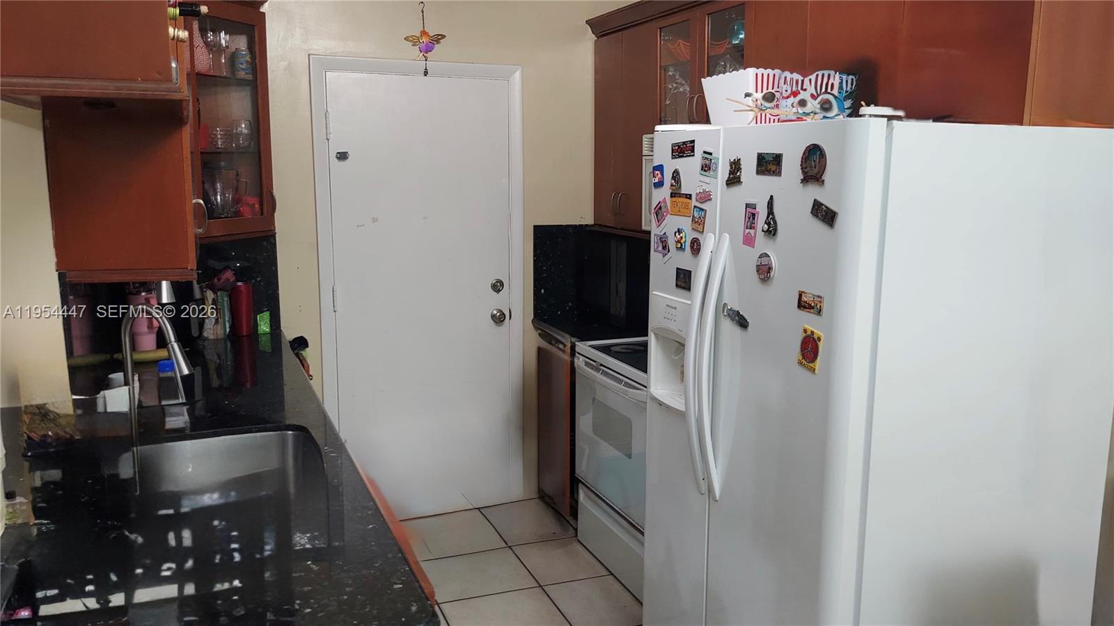 A kitchen features dark wood cabinets, black countertops, a white refrigerator, and a white door — 900 SW 84th Ave # 301E, Miami FL 33144, MIAMI, FL