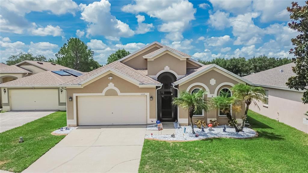 A single-story suburban house with a two-car garage, tan stucco exterior, and a landscaped yard — 11115 SILVER DANCER DRIVE, RIVERVIEW, FL