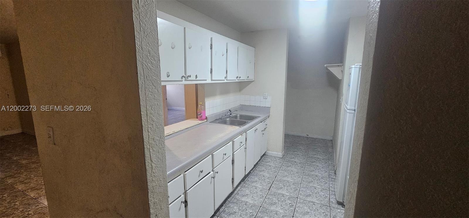 A galley-style kitchen features white cabinets, a gray countertop, and light-colored tile flooring — 3932 NW 207th St Rd, Miami Gardens FL 33055, MIAMI GARDENS, FL