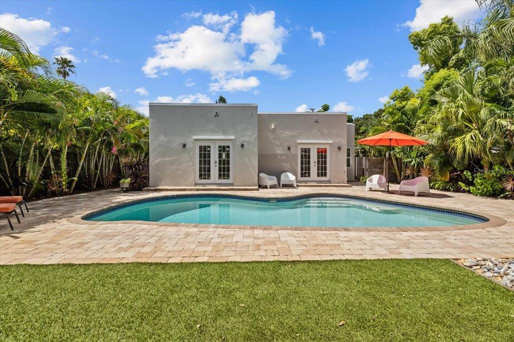 A backyard features a swimming pool, a paved patio, and a light-colored house with French doors — 219 N MISSOURI AVENUE, CLEARWATER, FL