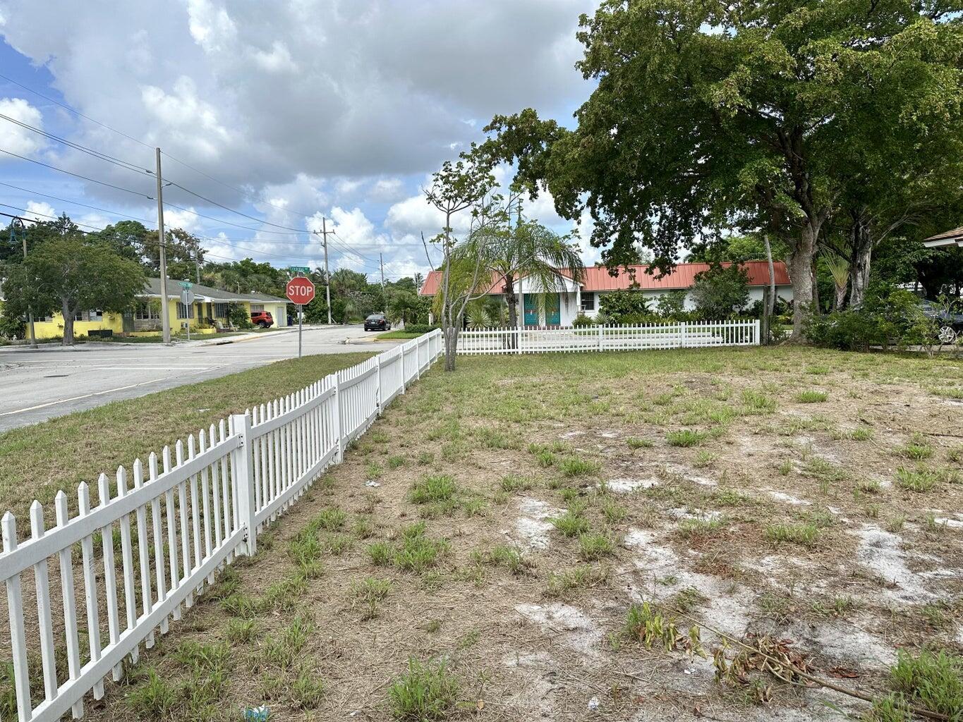 A white picket fence borders a vacant, grassy lot near a street intersection — 312 12th Avenue N, FL 33460, FL