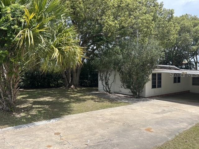 A concrete driveway leads to a single-story house with a carport and surrounding trees — 16815 SE 101ST COURT ROAD, SUMMERFIELD, FL