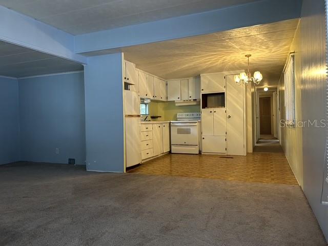 A kitchen with white cabinets and appliances opens to a carpeted living area — 16815 SE 101ST COURT ROAD, SUMMERFIELD, FL
