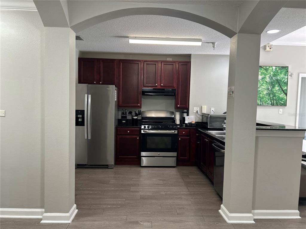 A kitchen features dark wood cabinets, stainless steel appliances, and wood-look flooring under an archway — 14501 GROVE RESORT AVENUE UNIT 1409, WINTER GARDEN, FL