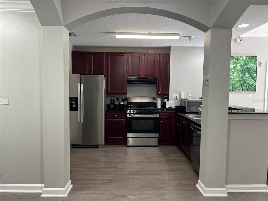 A kitchen features dark wood cabinets, stainless steel appliances, and wood-look flooring under an archway — 14501 GROVE RESORT AVENUE UNIT 1409, WINTER GARDEN, FL