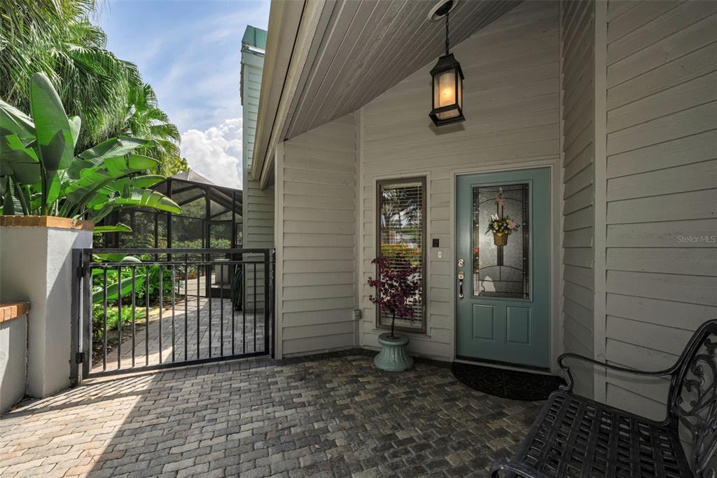 A paved front patio features a blue door, a hanging lantern, and a metal gate — 10497 LONGWOOD DRIVE, SEMINOLE, FL