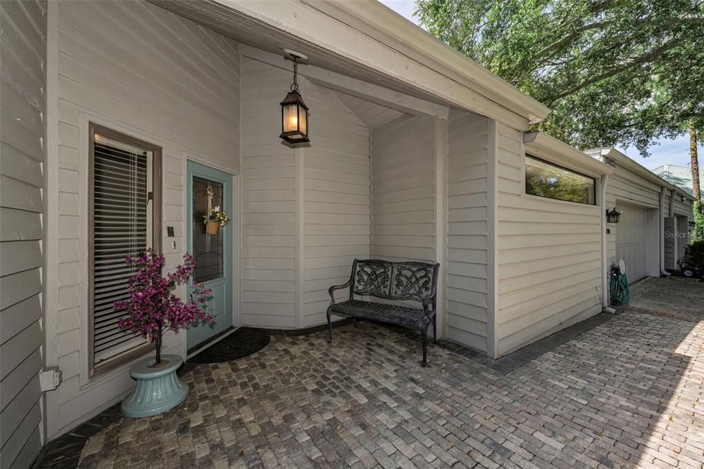 A light gray house exterior features a brick patio, a bench, and a light blue door — 10497 LONGWOOD DRIVE, SEMINOLE, FL