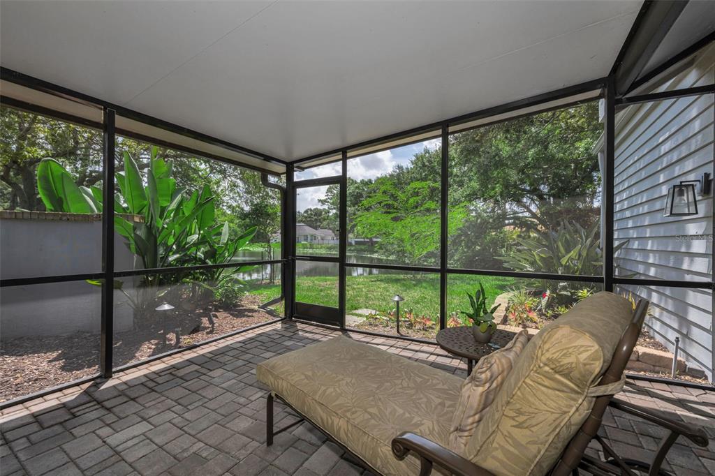 A screened-in patio with brick pavers overlooks a grassy yard and a pond — 10497 LONGWOOD DRIVE, SEMINOLE, FL