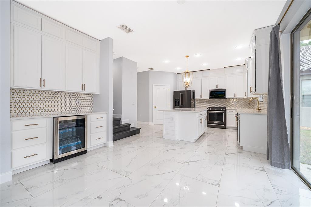 A modern kitchen features white cabinetry, marble-look tile floors, a center island, and stainless appliances — 163 ANCONA AVENUE, DEBARY, FL