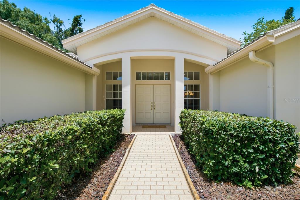 A paved walkway leads to the double front doors of a house with beige stucco — 3187 STERLING STREET, TARPON SPRINGS, FL