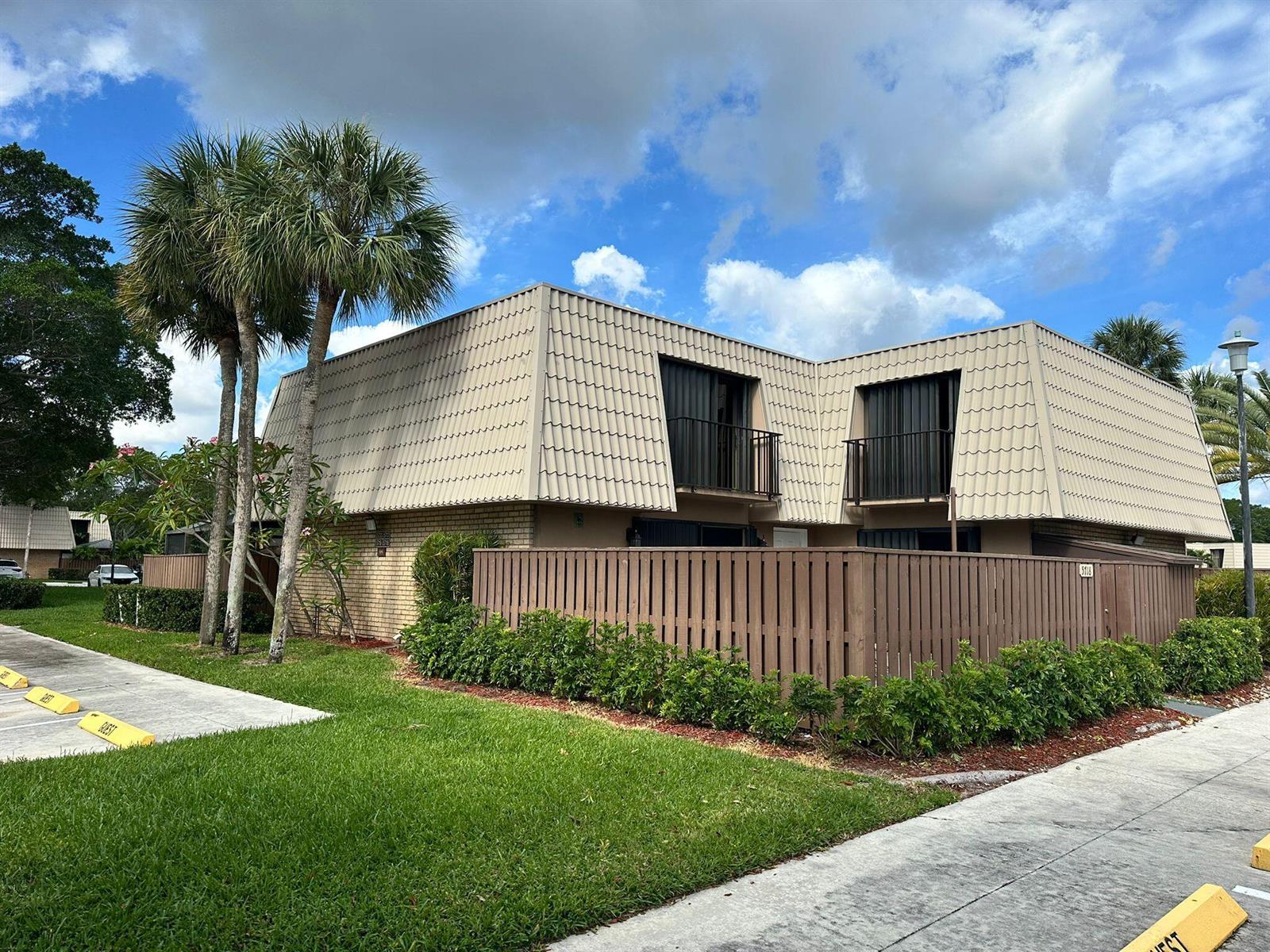 A two-story townhouse with a mansard roof, a wooden privacy fence, and palm trees — 5718 57th Way, West Palm Beach FL 33409, WEST PALM BEACH, FL