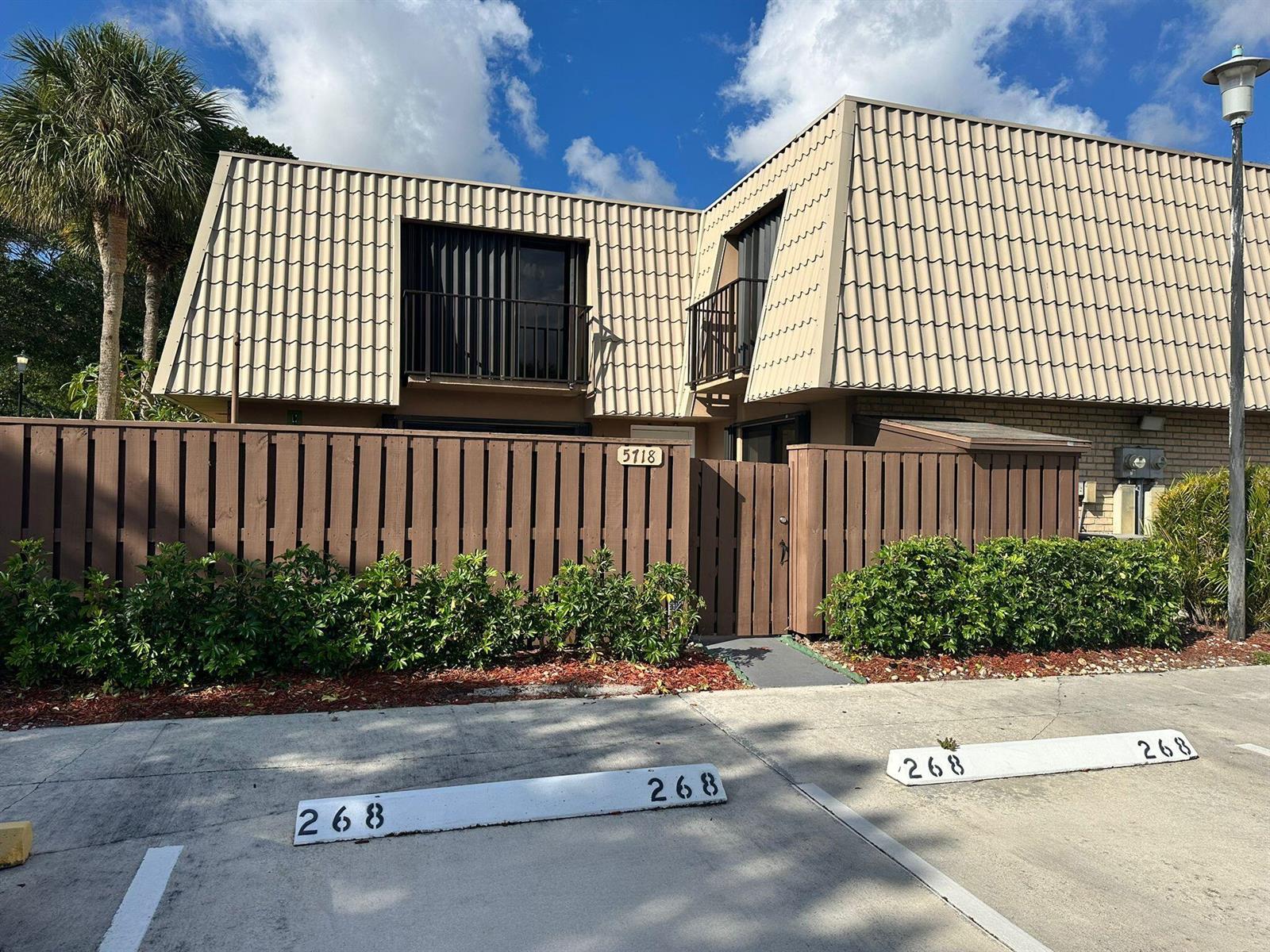 A two-story townhouse with a mansard roof, brown wooden fence, and assigned parking spaces — 5718 57th Way, West Palm Beach FL 33409, WEST PALM BEACH, FL