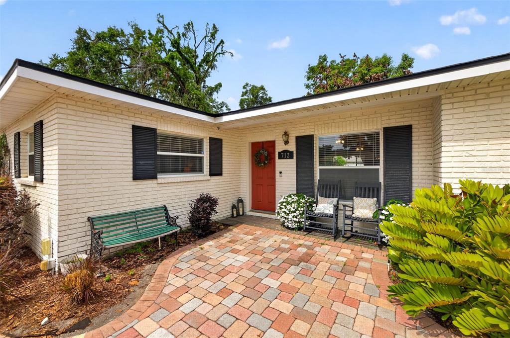 A brick house exterior features a red front door, a paver patio, and rocking chairs — 712 S OAKWOOD AVENUE, BRANDON, FL