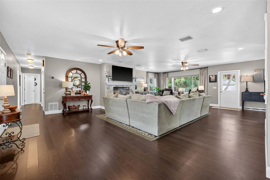 A spacious living room features dark hardwood floors, a large sectional sofa, and a fireplace — 712 S OAKWOOD AVENUE, BRANDON, FL