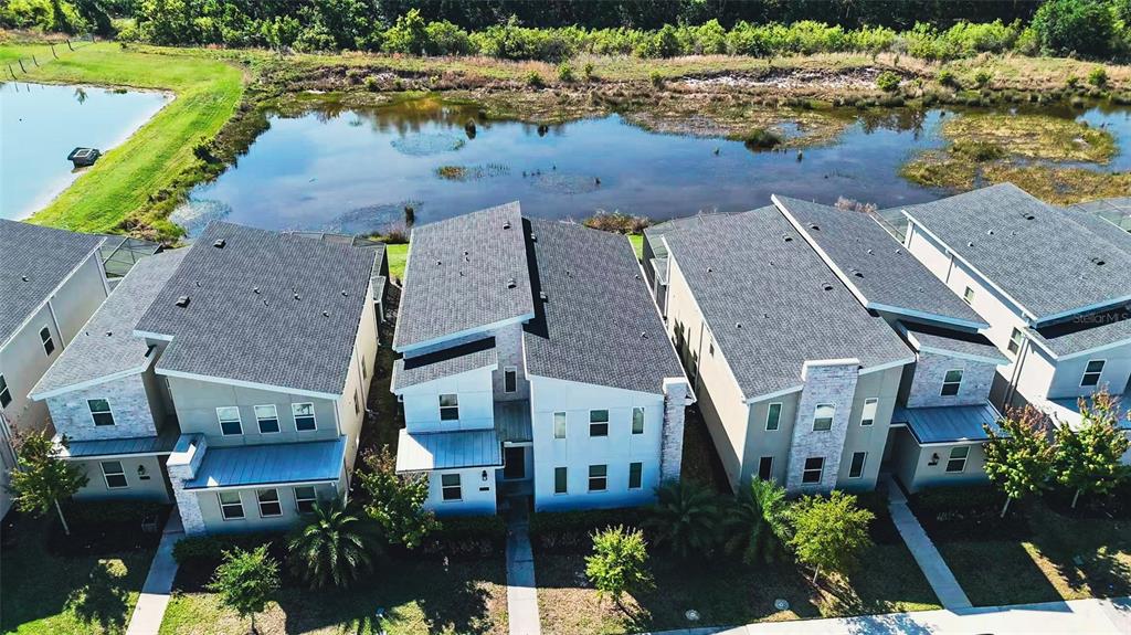 An aerial view shows a row of modern townhomes situated next to a pond — 2981 PROTAGONIST STREET, KISSIMMEE, FL