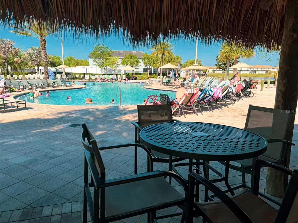 A patio with a round metal table and chairs overlooks a community swimming pool — 2981 PROTAGONIST STREET, KISSIMMEE, FL