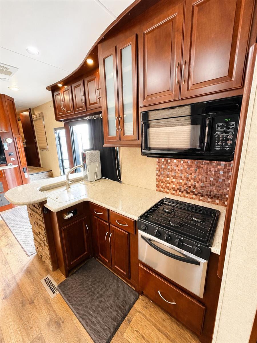A kitchen in an RV features cherry wood cabinets, a gas stove, and a microwave — 14130 SE 126th Boulevard, Okeechobee FL 34974, OKEECHOBEE, FL