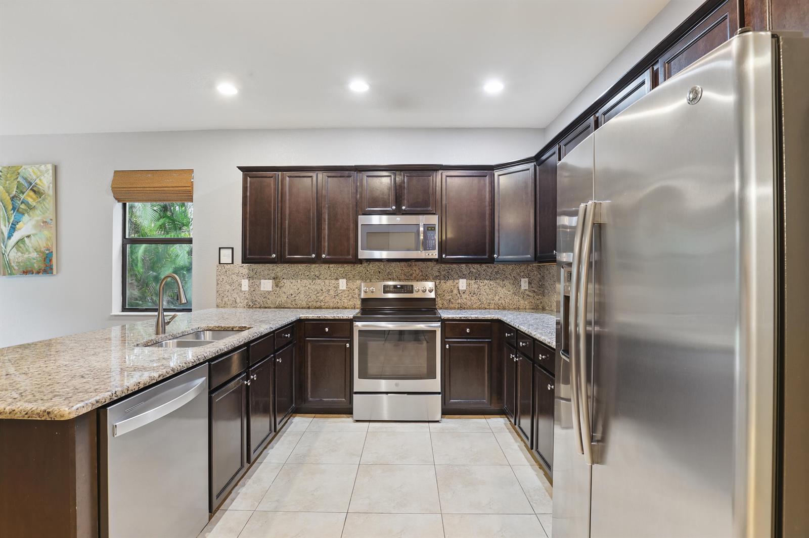 A kitchen features dark wood cabinets, granite countertops, stainless steel appliances, and tile flooring — 3801 Aspen Leaf Drive, Boynton Beach FL 33436, BOYNTON BEACH, FL