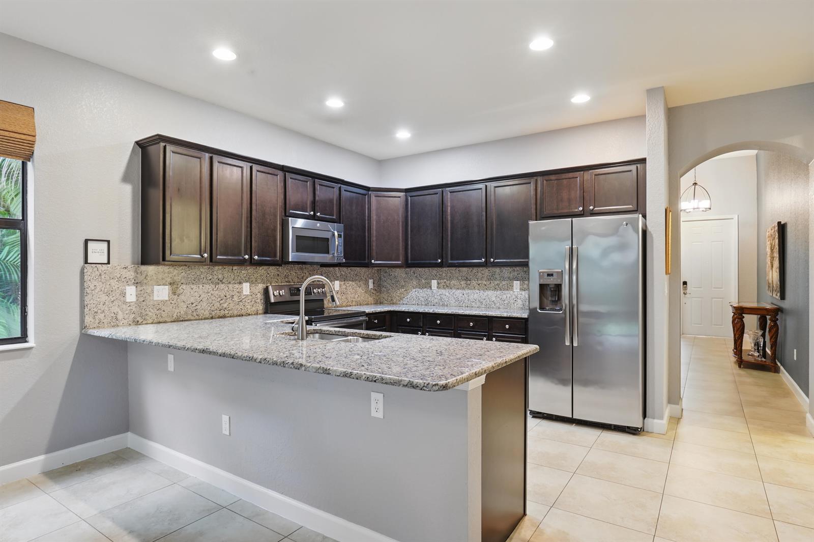 A kitchen features dark wood cabinets, granite countertops, stainless steel appliances, and tile flooring — 3801 Aspen Leaf Drive, Boynton Beach FL 33436, BOYNTON BEACH, FL