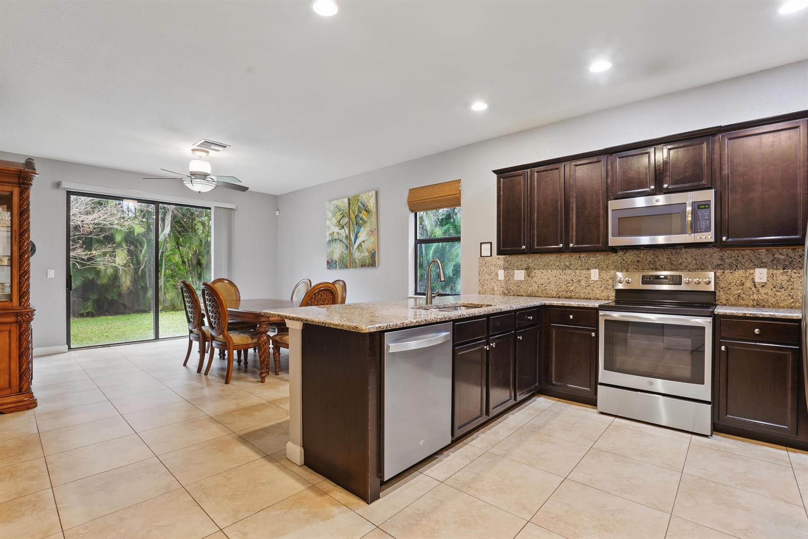 A kitchen with dark wood cabinets, granite countertops, and stainless steel appliances opens to a dining area — 3801 Aspen Leaf Drive, Boynton Beach FL 33436, BOYNTON BEACH, FL