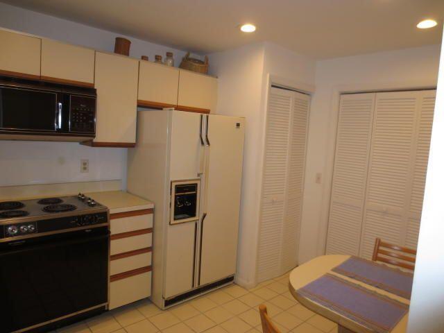 A kitchen features white cabinets, a black stove, a white refrigerator, and a small table — 7535 La Paz Boulevard # 307, Boca Raton FL 33433, BOCA RATON, FL