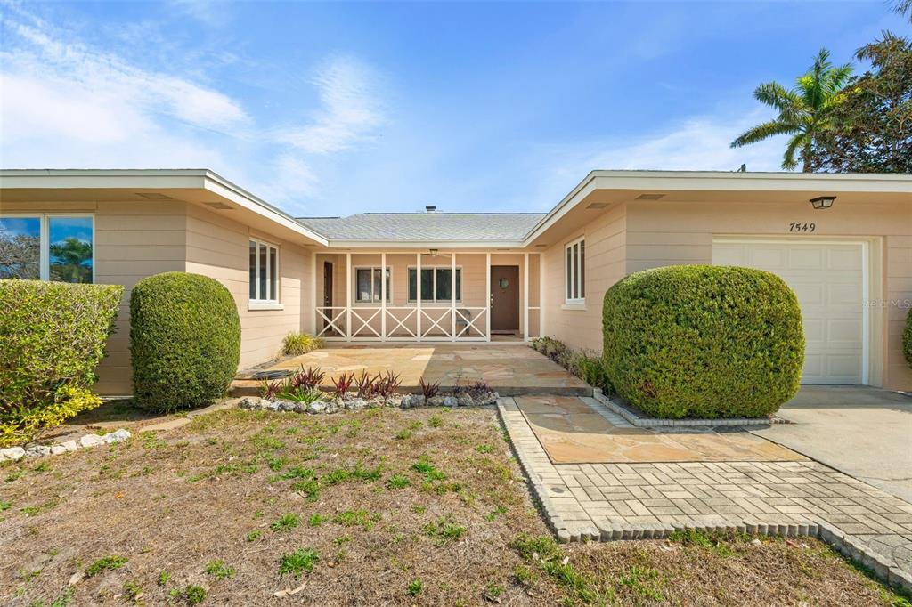 A single-story house with a beige exterior, a stone patio, and two large round bushes — 7549 WESTMORELAND DRIVE, SARASOTA, FL