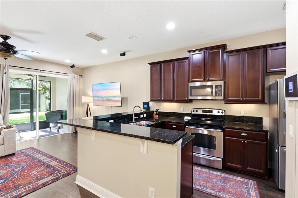 A kitchen with dark wood cabinets and granite countertops overlooks a living area with patio doors — 5415 VIA APPIA WAY, SANFORD, FL