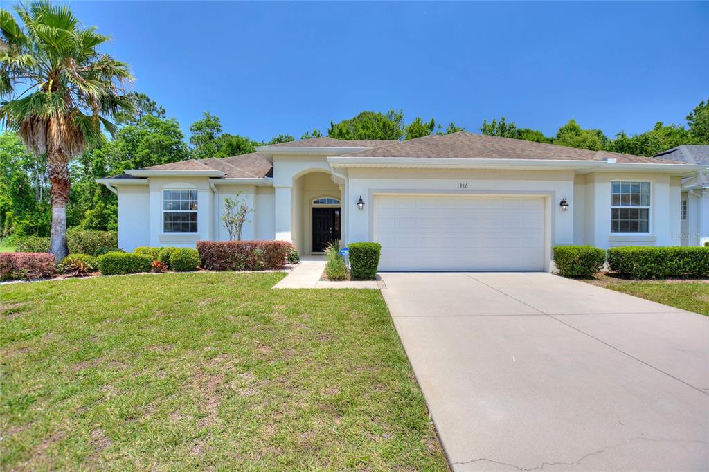 A single-story house with a white stucco exterior, a two-car garage, and a palm tree — 1316 GOLF COURSE PARKWAY, DAVENPORT, FL