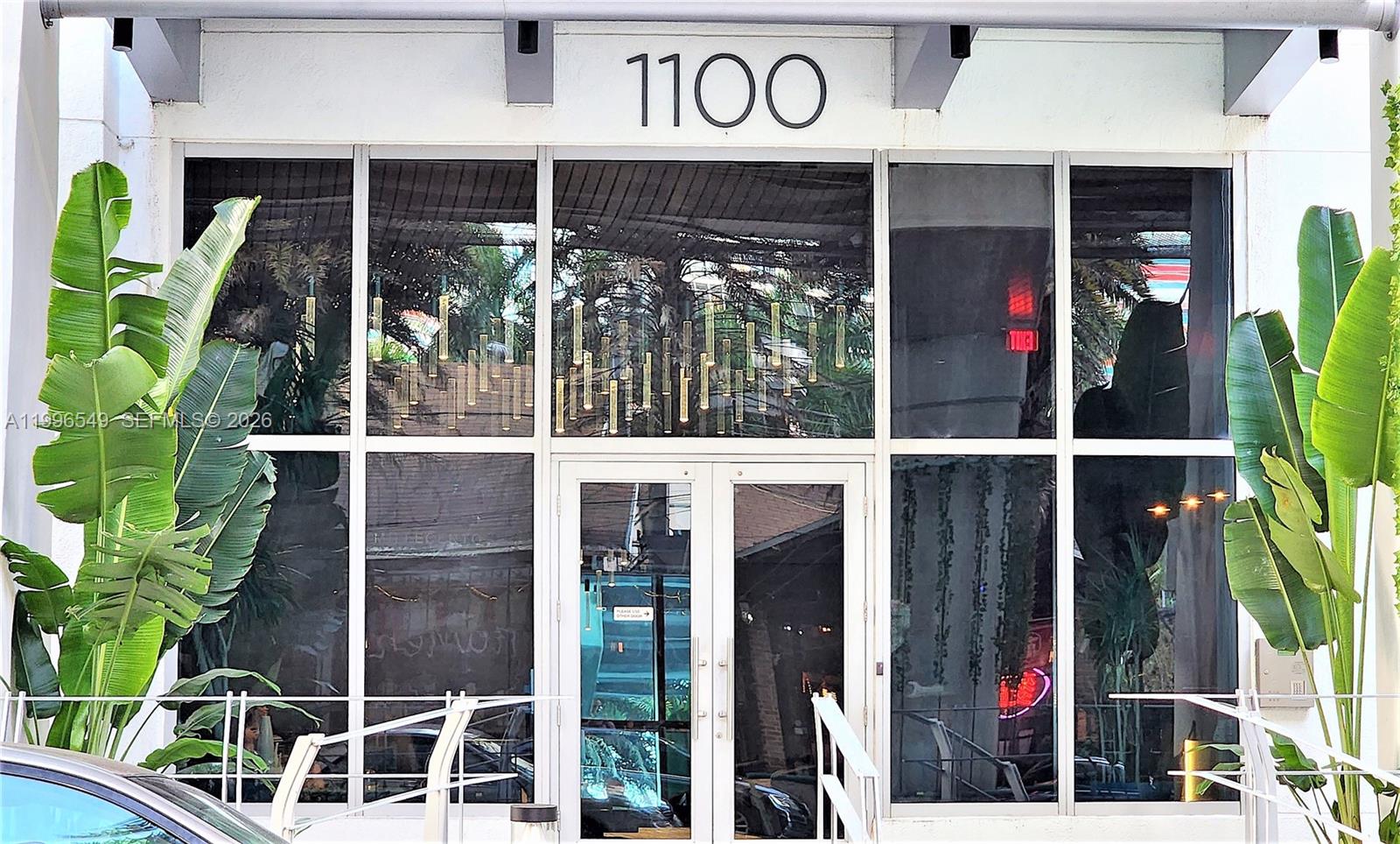 The exterior entrance of a building features glass doors, large windows, and potted banana plants — 1100 S Miami Ave # 1906, Miami FL 33130, MIAMI, FL