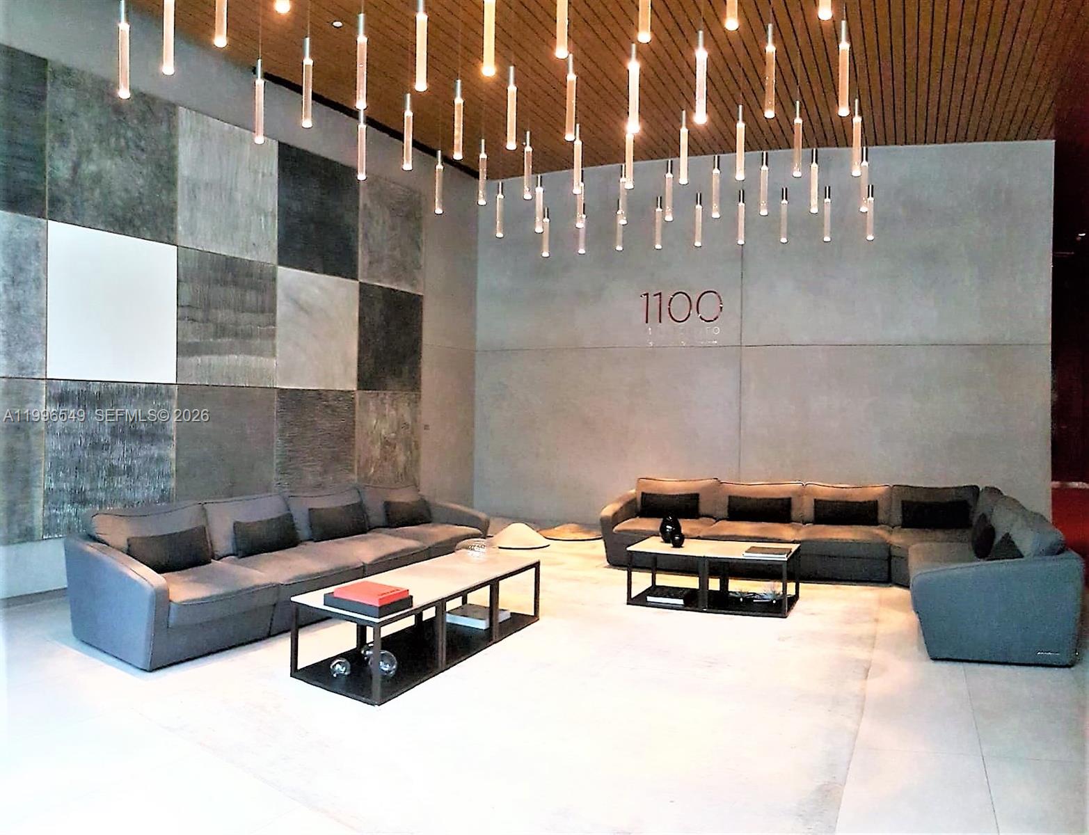 A modern lobby features two gray sectional sofas, low coffee tables, and hanging pendant lights — 1100 S Miami Ave # 1906, Miami FL 33130, MIAMI, FL