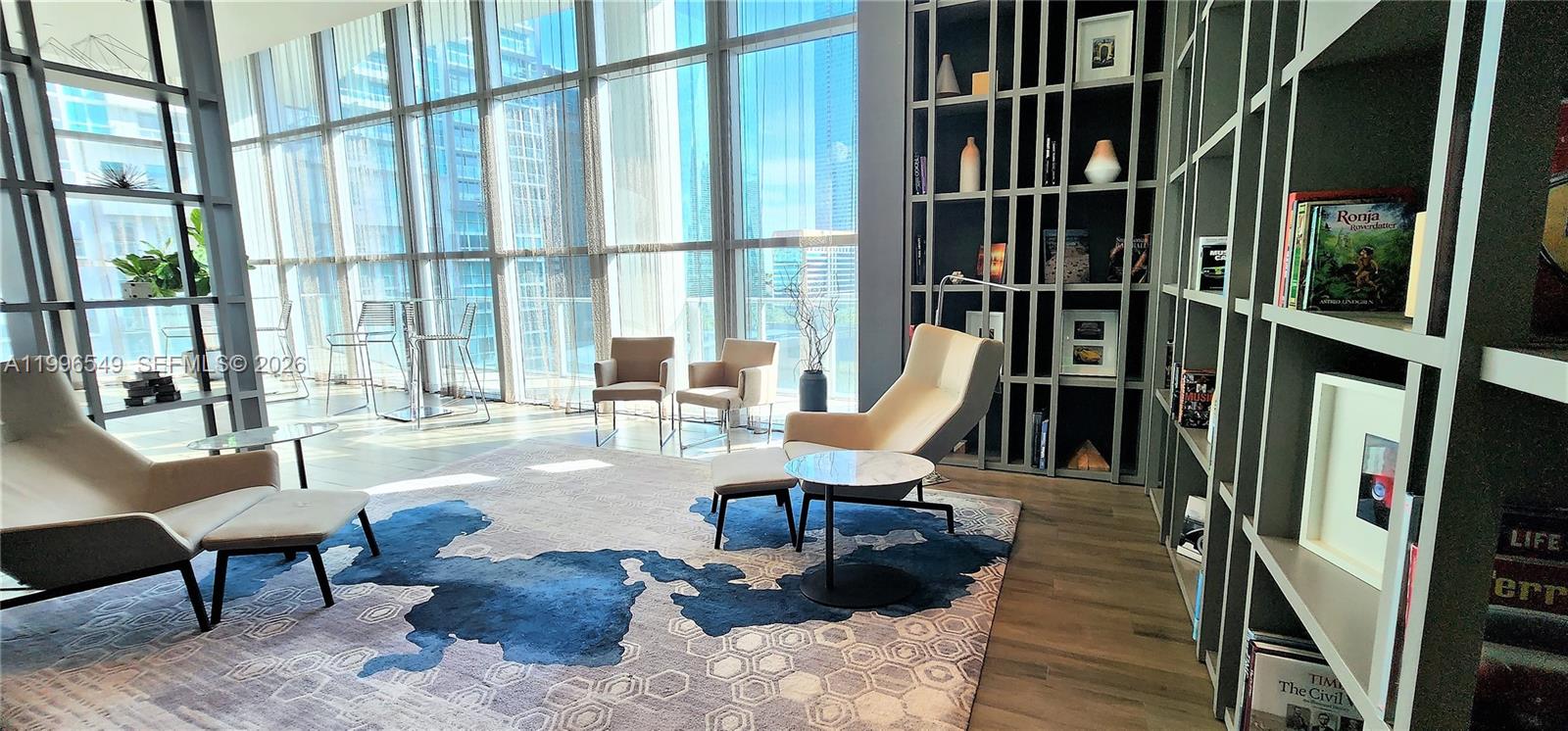 A modern living room features floor-to-ceiling windows, two lounge chairs with ottomans, and built-in shelving — 1100 S Miami Ave # 1906, Miami FL 33130, MIAMI, FL