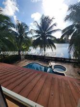 An elevated view of a swimming pool and spa overlooking a lake with palm trees — 2614 NE 41st Rd, Homestead FL 33033, HOMESTEAD, FL
