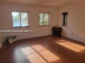 An empty room with wood-look flooring, three windows, and a small dark wooden cabinet — 2614 NE 41st Rd, Homestead FL 33033, HOMESTEAD, FL