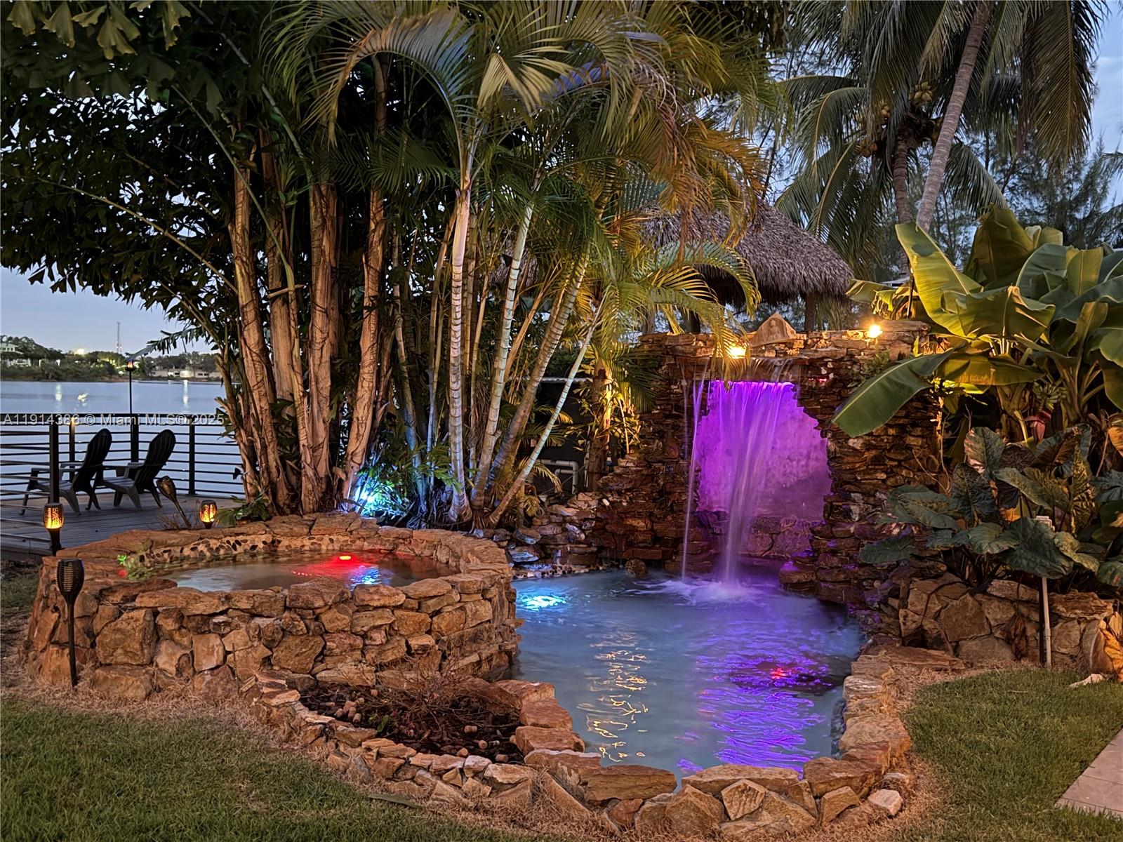 A stone hot tub and waterfall pond are illuminated by colorful lights in a tropical backyard — 7521 SW 56th St, Miami FL 33155, MIAMI, FL