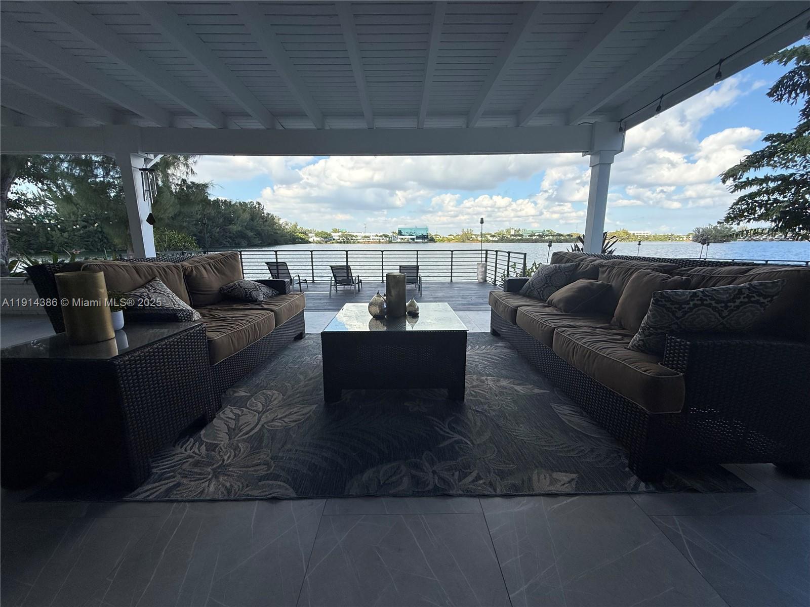 A covered outdoor patio features two wicker sofas, a coffee table, and a waterfront view — 7521 SW 56th St, Miami FL 33155, MIAMI, FL
